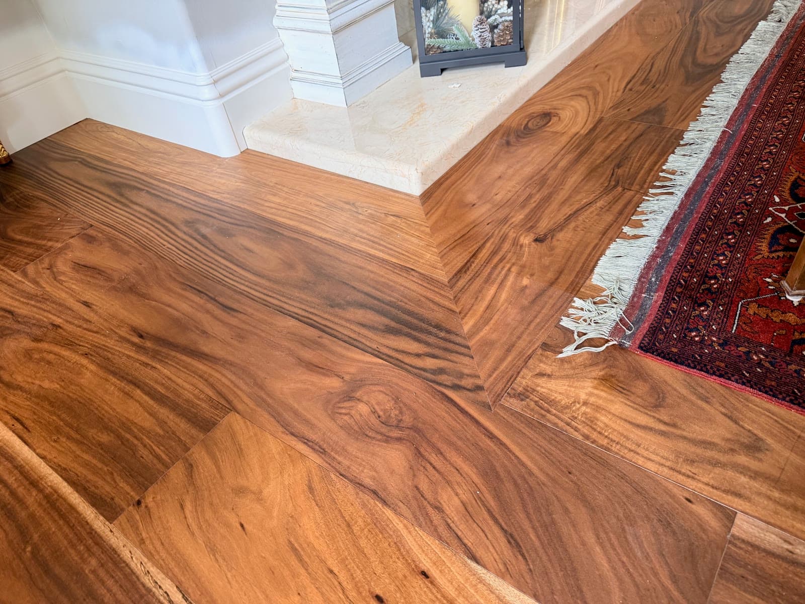 Highly figured acacia plank floor with a mitered border at a travertine hearth, Carmel Valley