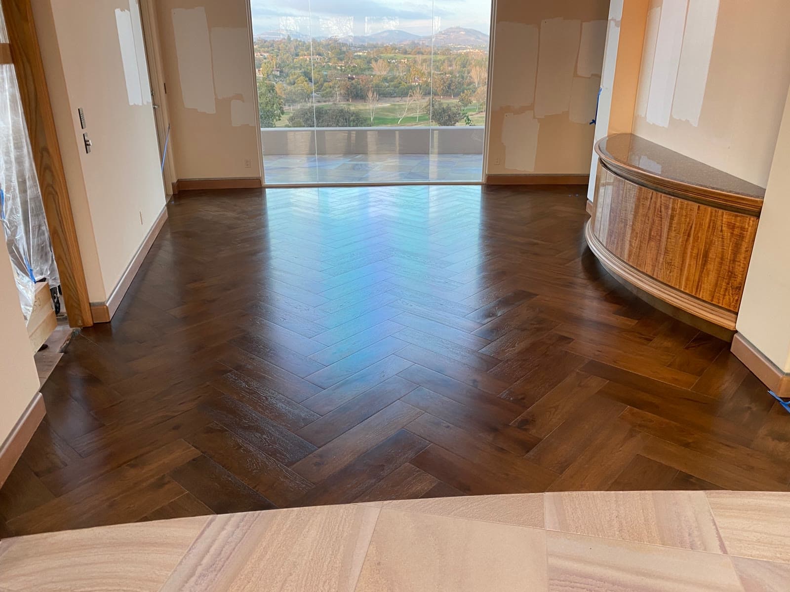 Dark-stained herringbone wood floor meeting a stone tile entry in a Rancho Santa Fe living room with a valley view