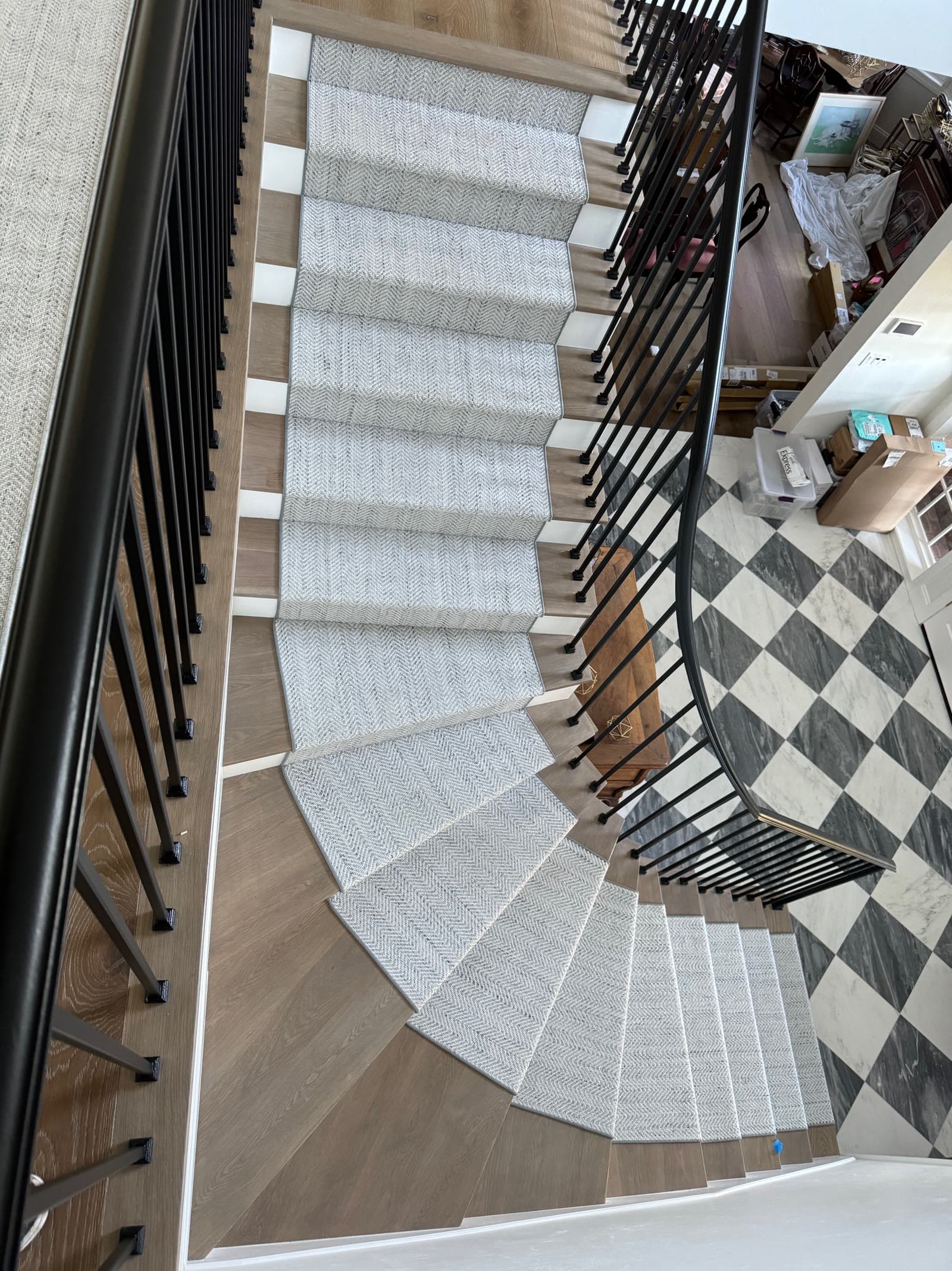 White oak staircase and runner spiraling down to a marble checkerboard entry floor