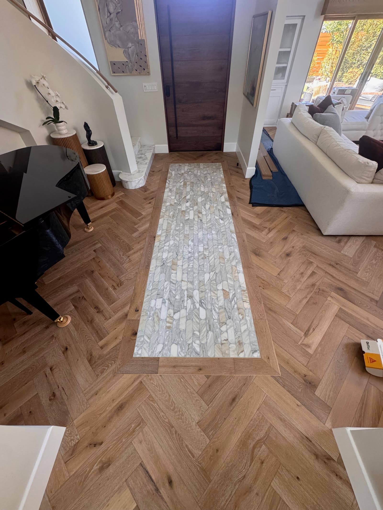 Rancho Santa Fe entry hall in herringbone white oak with a marble mosaic runner leading to a walnut front door