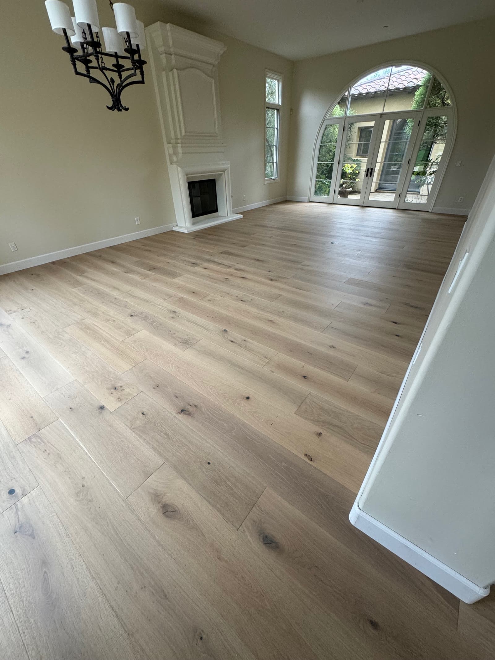 Light wide-plank white oak floor in a Santaluz room with a limestone fireplace and arched French doors