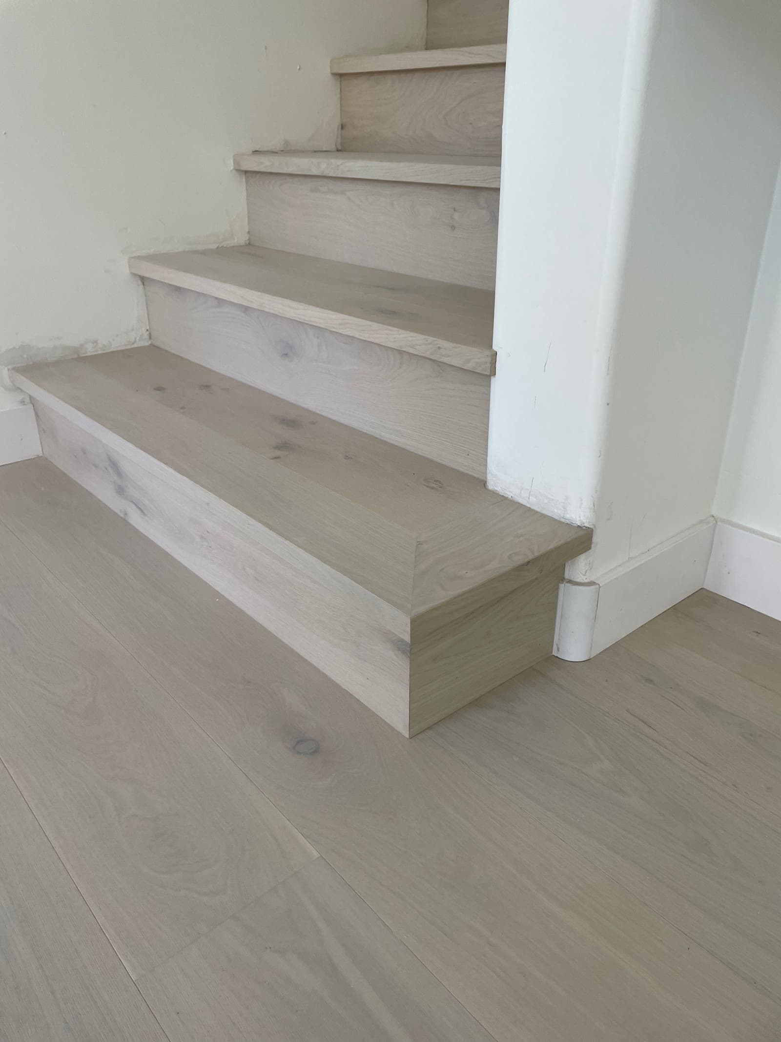 Mitered return on a limed oak bottom step beside a wide-plank oak floor