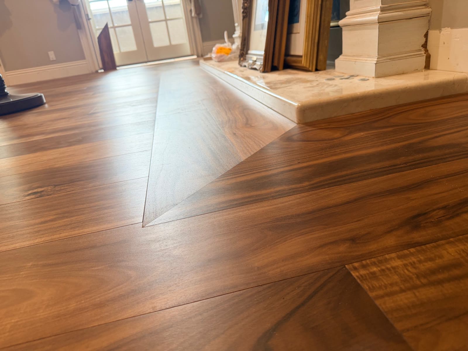Acacia plank floor with a mitered diagonal seam meeting a marble hearth