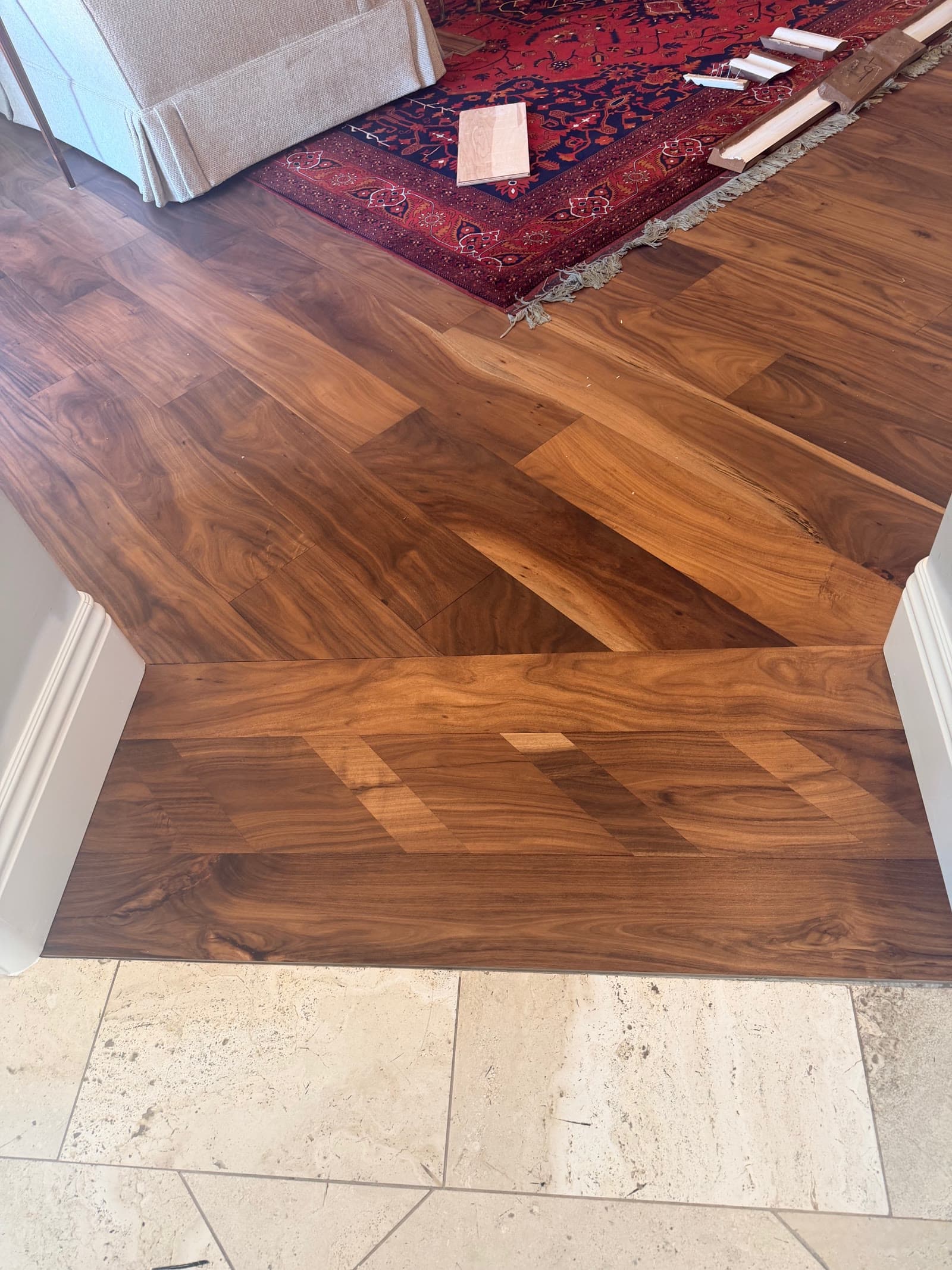 Wide-plank acacia floor stepping down to travertine at a room threshold