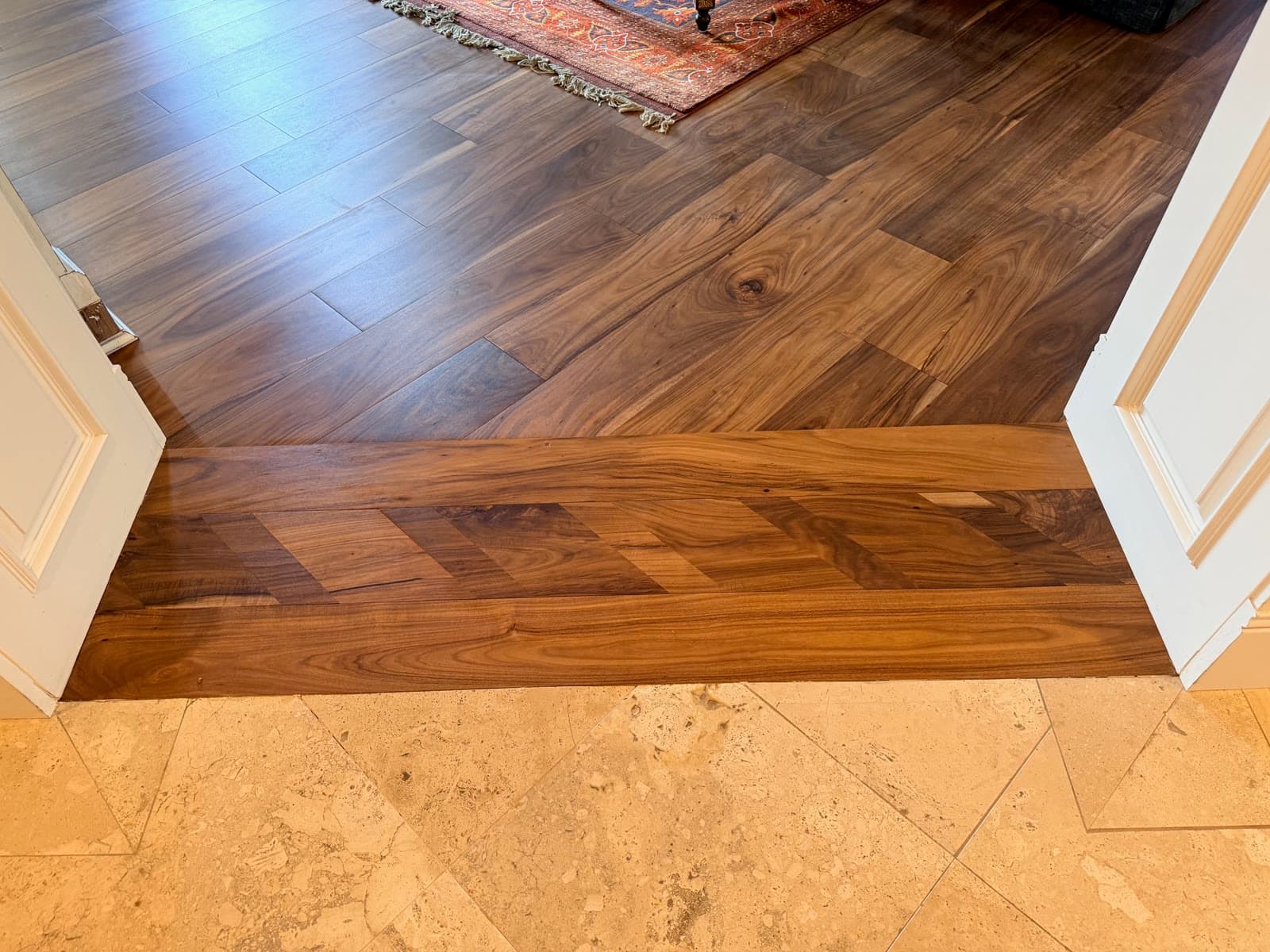 Acacia plank floor finished tight to a travertine tile floor at a paneled door