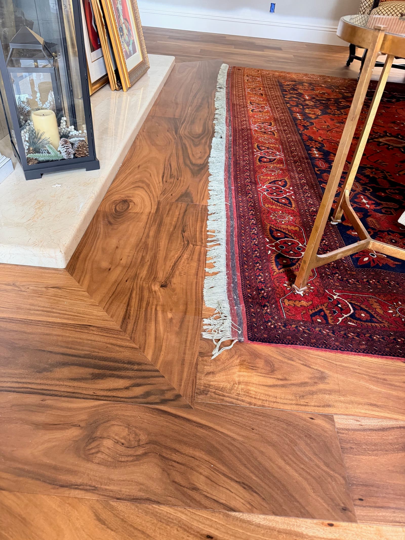 Acacia hardwood laid in a mitered pattern beside a travertine hearth and Persian rug