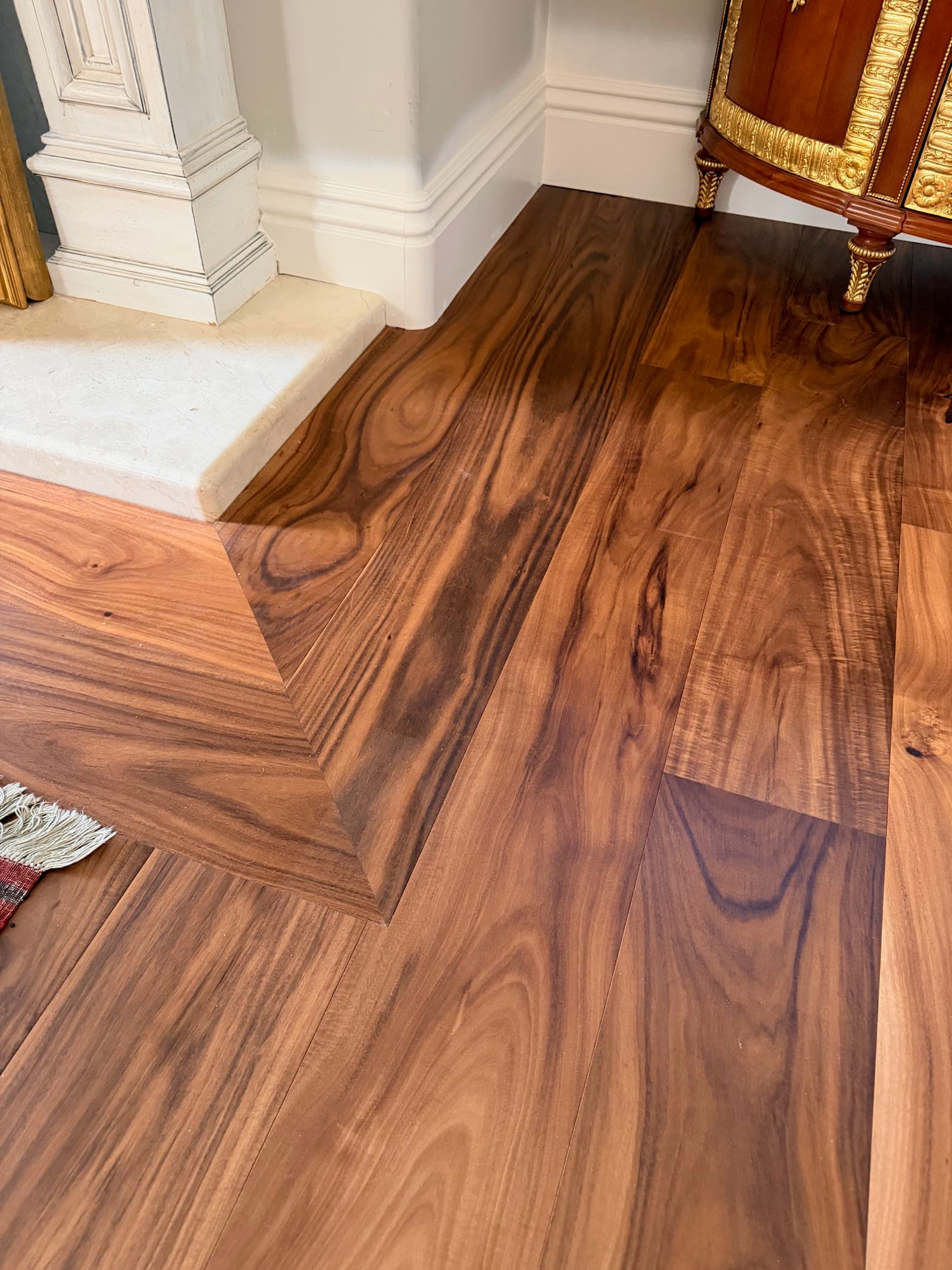 Close view of acacia grain and a mitered border beside a limestone hearth step