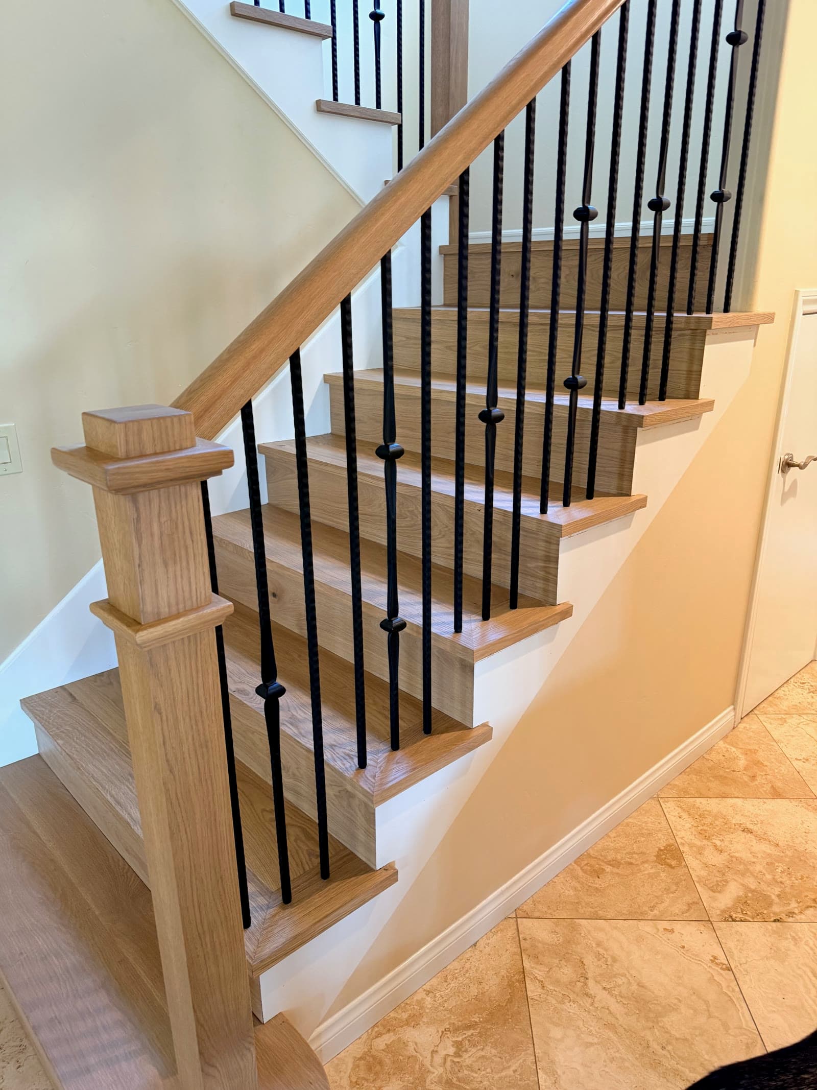 White oak staircase from the side showing mitered tread returns and black iron balusters