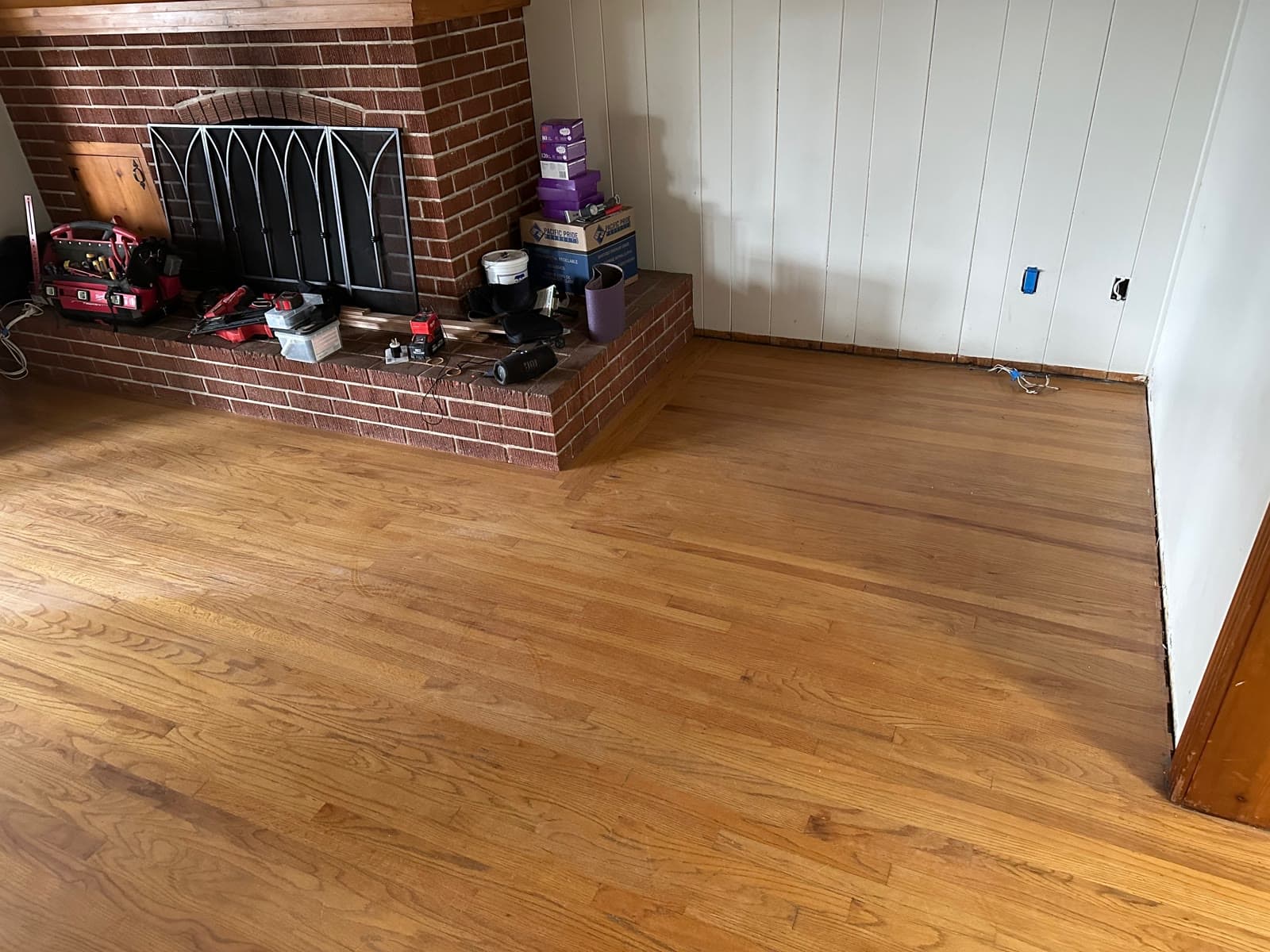 Worn red oak strip floor in a La Jolla room with a brick fireplace, before refinishing