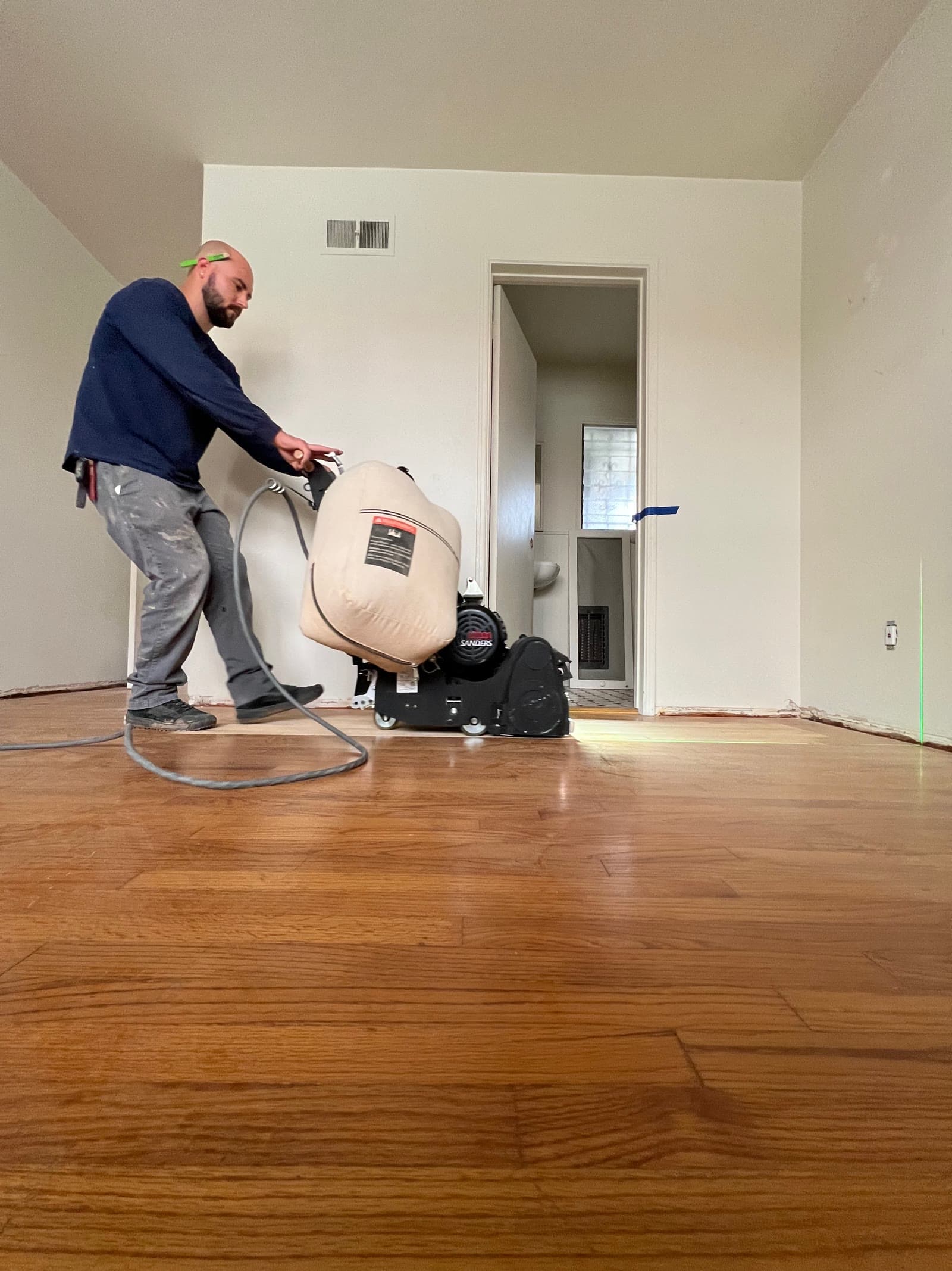 Stone Peters running a drum sander across a red oak floor in La Jolla