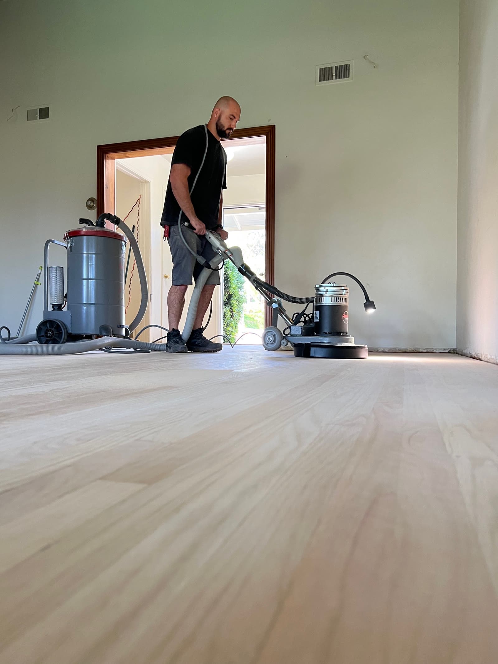 Installer running a buffer with a dust extractor over a freshly sanded floor in La Jolla