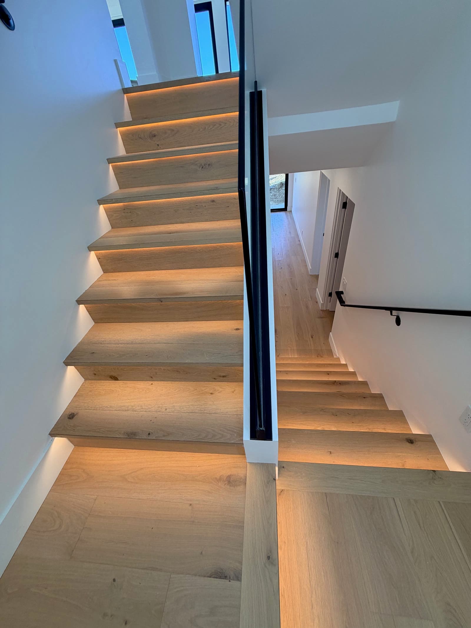 Lit white oak staircase seen from above, with a black steel handrail and oak landing