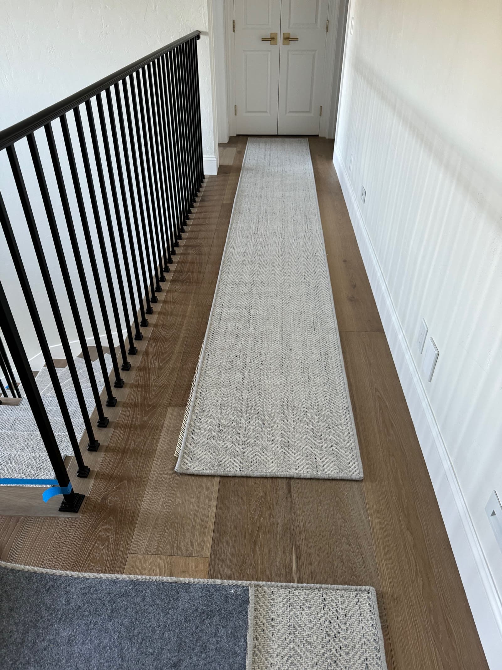Upstairs hallway in wide-plank white oak with a wool runner and black iron balustrade