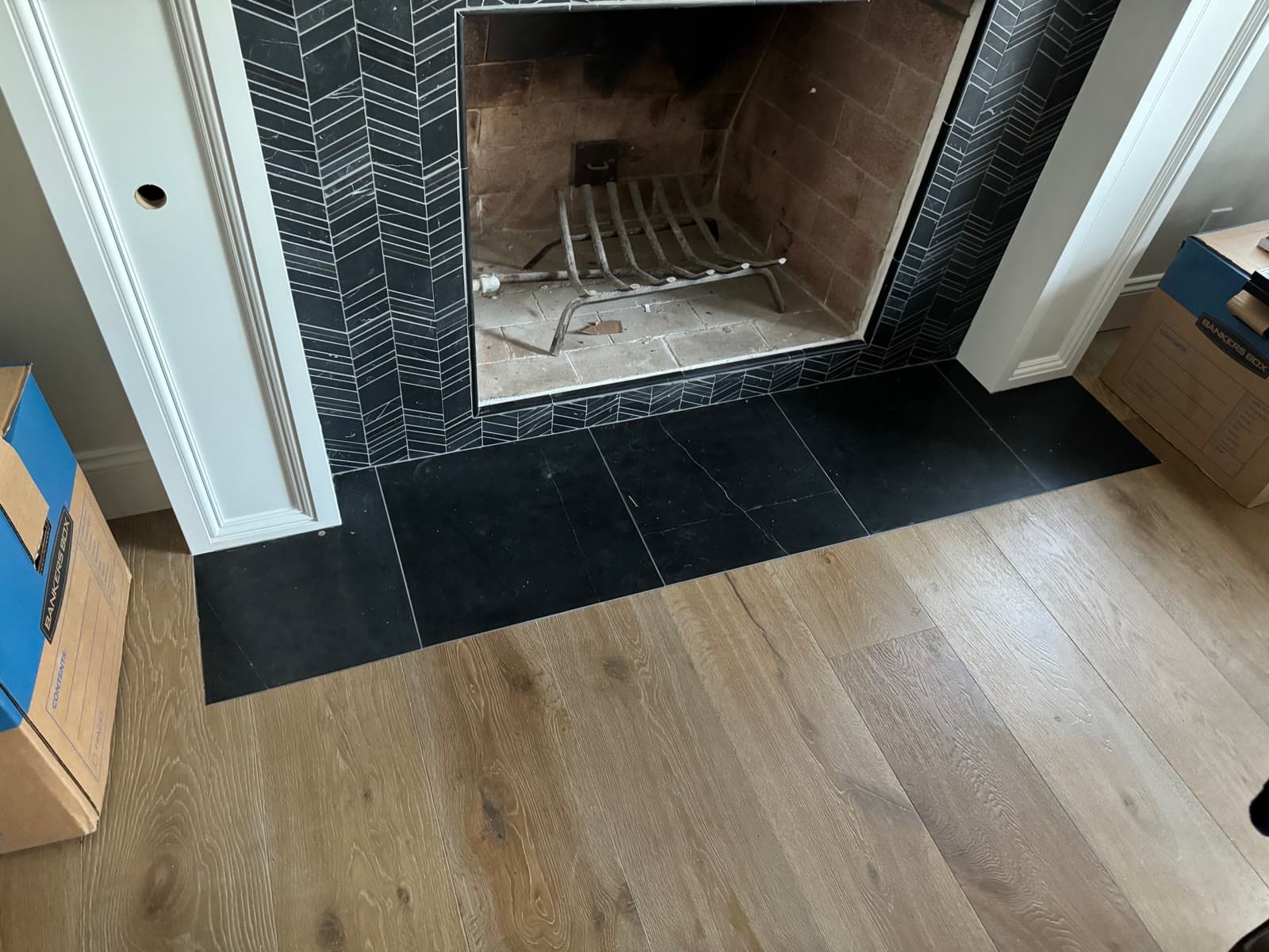 Wide-plank white oak floor meeting a black slate hearth under a chevron-tiled fireplace