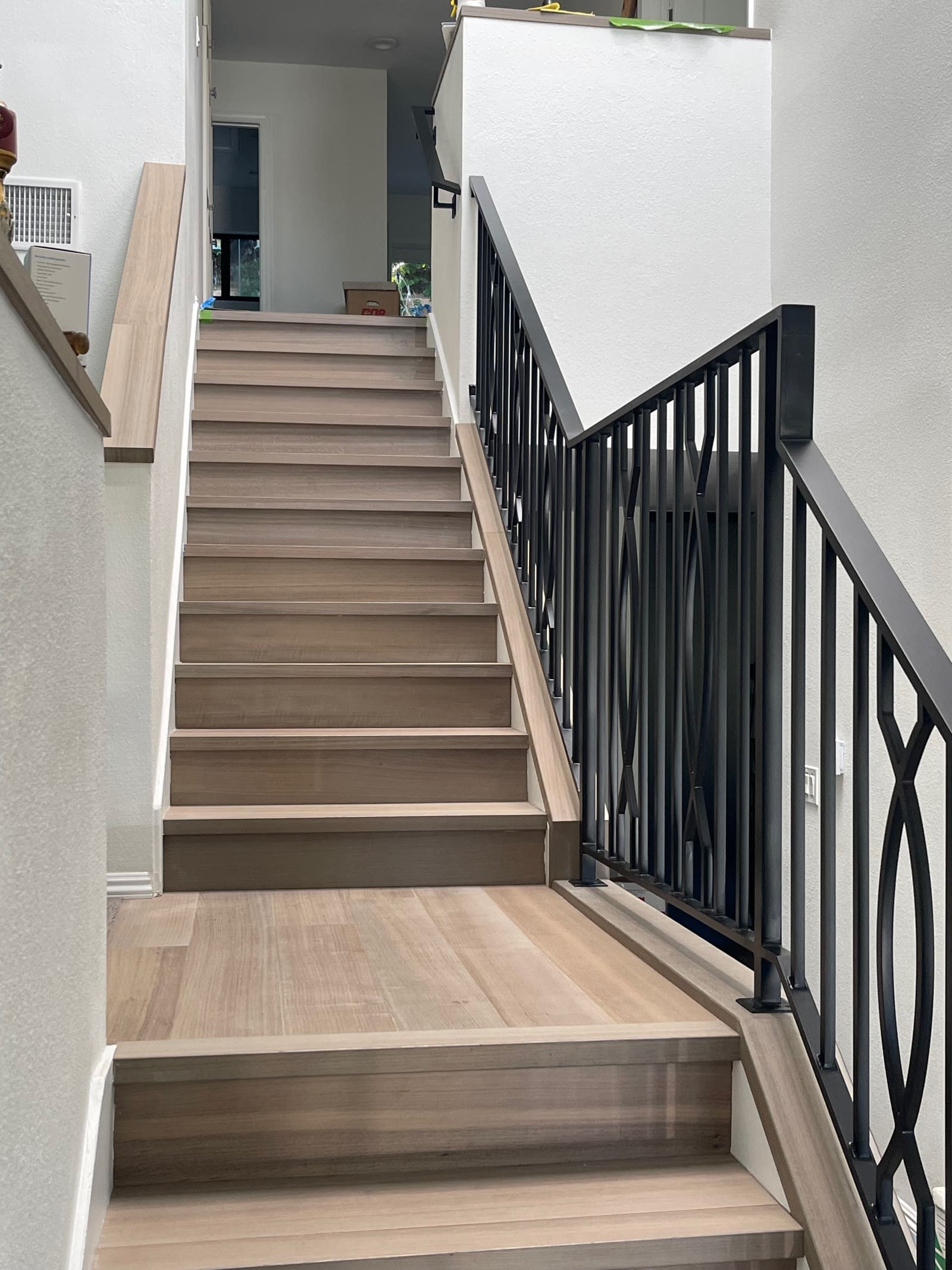 Finished pale plank staircase with patterned black metal balusters in San Diego