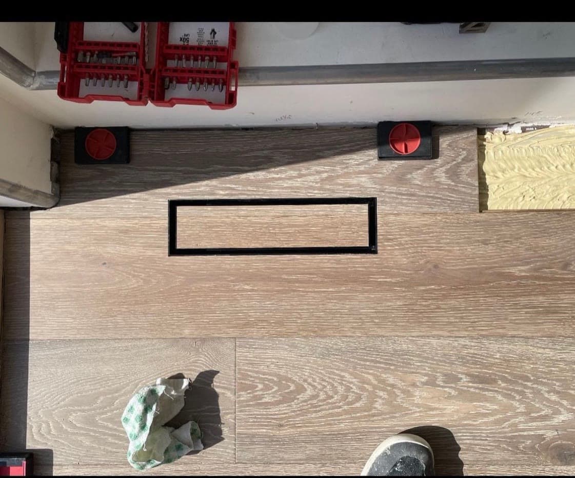 Black linear floor vent set flush into a white oak plank floor