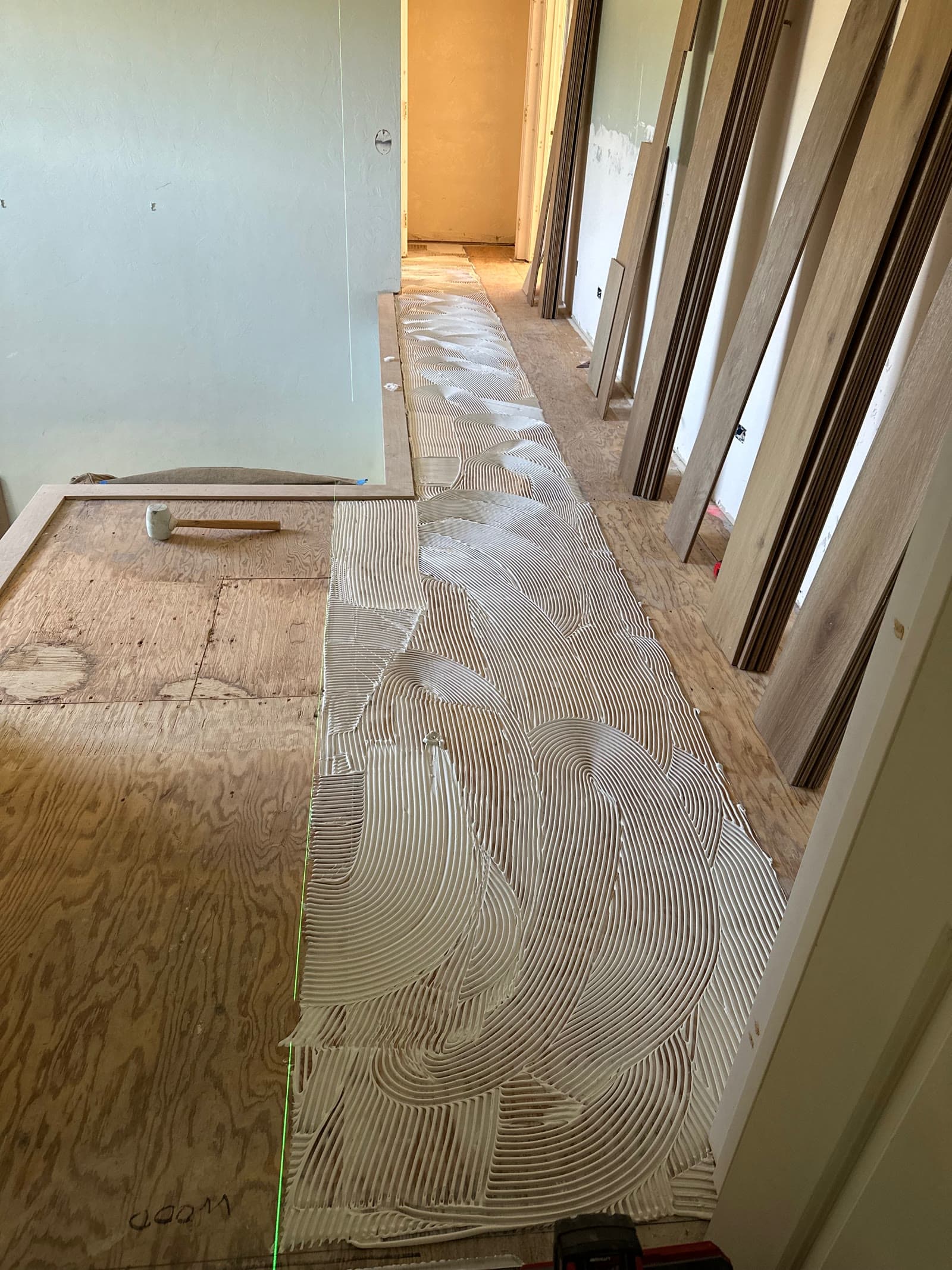 Notched trowel adhesive combed over a plywood subfloor with plank stacked ready to lay