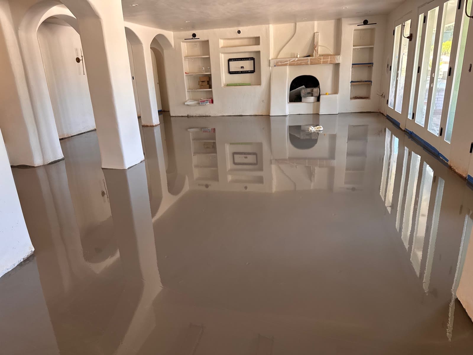 Self-leveling underlayment poured across a large Spanish-style room with arches and a beehive fireplace