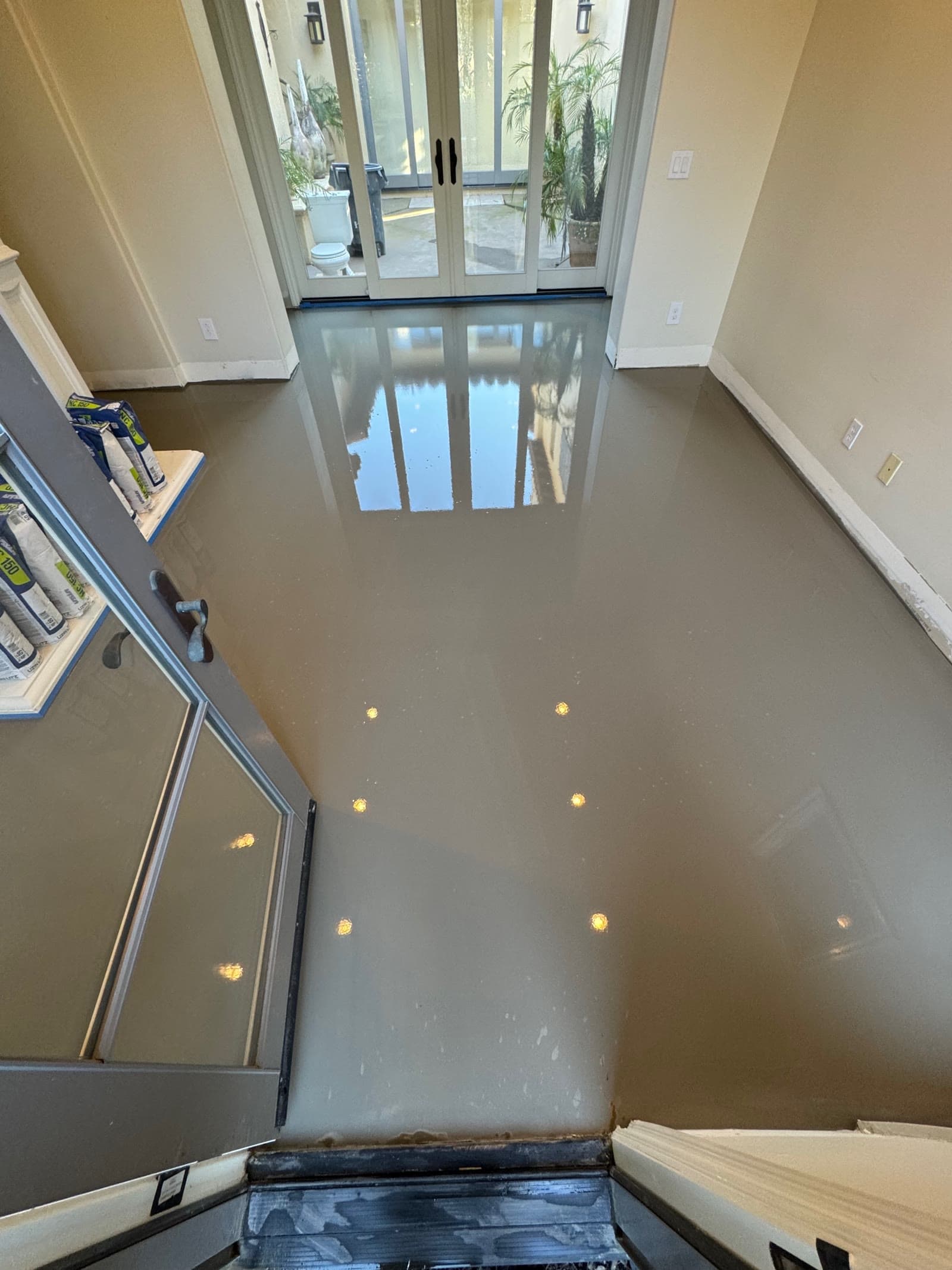 Gray self-leveling underlayment curing in a Santaluz entry with French doors to a courtyard